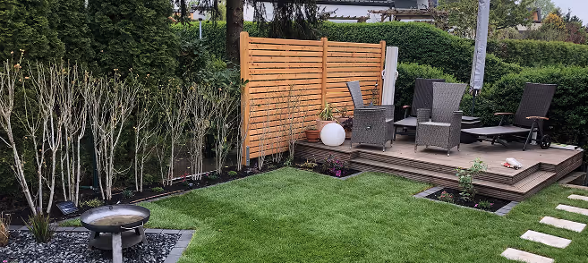 Gut gepflegter Garten mit Rasenfläche, Holzterrasse, Gartenmöbeln und Hecke im Hintergrund.