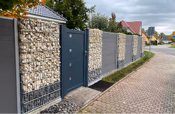 Moderner Gartenzaun aus Drahtkörben mit Steinen gefüllt und dunklen Metallpaneelen neben einem gepflasterten Gehweg.