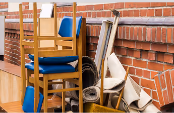 Gestapelte blaue Stühle und zusammengerollte Teppiche lehnen an einer roten Backsteinwand.