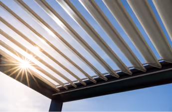 Sonnenschein durch die Lamellen einer modernen Pergola unter blauem Himmel.