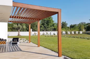 Holzpergola auf einer Terrasse mit Blick auf einen gepflegten Garten und blauen Himmel.