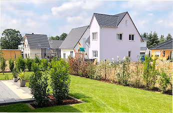Reihenhaus mit gepflegtem Vorgarten, grünem Rasen und Sträuchern unter blauem Himmel.