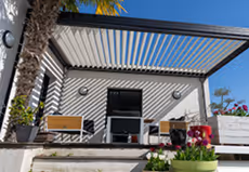 Moderner Außenbereich mit Pergola, zwei Stühlen, Tisch und Pflanzen auf einer Terrasse.