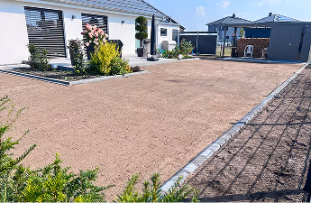 Großer leerer Gartenplatz mit Kies vor modernen weißen Häusern und blühenden Pflanzen an einem sonnigen Tag.