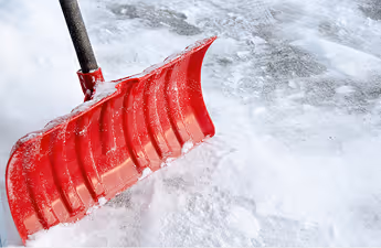 Roter Schneeschieber schaufelt Schnee auf einer schneebedeckten Fläche.